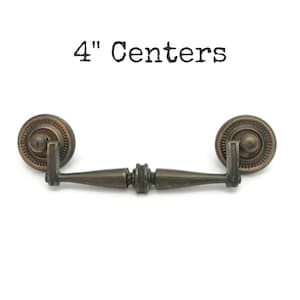 May include: Antique bronze drawer pull with a decorative circular design on each end. The pull has a 4-inch (10.16 cm) center-to-center measurement, with the text "4" Centers" above the pull.