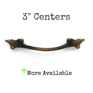 May include: A bronze-colored cabinet pull with ornate leaf detailing. The pull is 3 inches (7.6 cm) center to center, with the text "3" Centers" above and "More Available" below.