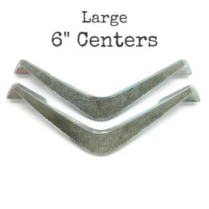 May include: Two silver, 6-inch center, V-shaped cabinet pulls with a textured finish.  Large.