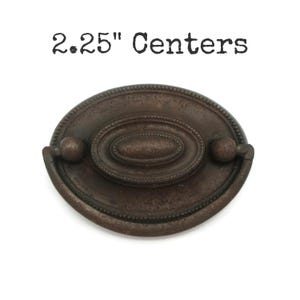 May include: A 2.25" center oval cabinet pull with a brown finish and a decorative design.