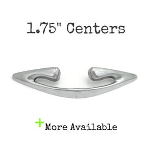 May include: A silver-colored cabinet pull with a curved design. The text "1.75" Centers" is above the pull, and "More Available" is below. The pull measures 1.75 inches between the centers of the mounting holes.