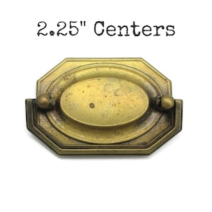 May include: An antique brass drawer pull with an octagonal backplate and a central oval handle. The metal has a weathered, tarnished finish with visible patina. The text 2.25" Centers is printed above the hardware, indicating the mounting distance.