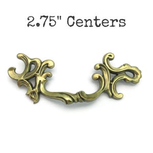 May include: Ornate brass-toned drawer pull with a curved handle and decorative scrollwork. The text "2.75" Centers" is above the pull. This vintage-style hardware is designed for furniture restoration or adding a classic touch to cabinets.