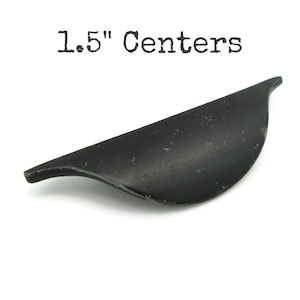 May include: A black, curved cabinet pull with a matte finish. The text "1.5" Centers" is printed above the pull. The pull is approximately 1.5 inches in length, designed for furniture hardware.