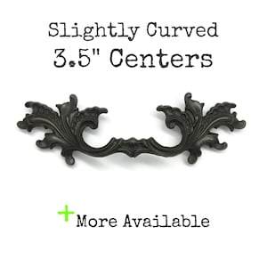 May include: A dark metal drawer pull with an ornate, scrolling design and a slightly curved shape. The text above reads Slightly Curved 3.5" Centers, and the text below reads + More Available.