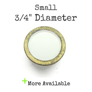 May include: Small, round button with a 3/4" diameter. The button has a white center and a gold-colored, slightly aged metal rim. The text "More Available" is below the button.