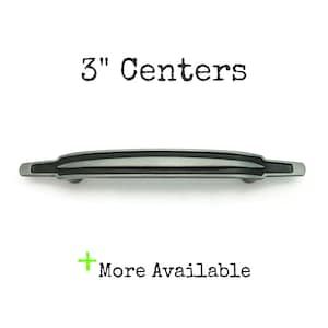 May include: A silver-toned cabinet pull with a black stripe detail. The pull is 7.6 cm in centre-to-centre measurement.  "3" Centers" is written above the pull.