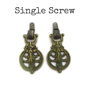 May include: Two antique brass drawer pulls with an ornate, floral design. The pulls have a dark, aged patina and a single screw attachment. The text "Single Screw" is above the pulls.
