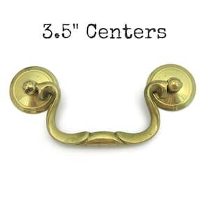 May include: A brass-toned drawer pull with a curved handle and circular backplates. The text "3.5" Centers" is above the pull. The hardware is designed for furniture and has a vintage aesthetic.