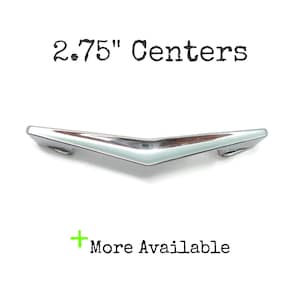 May include: A polished chrome cabinet pull with a V-shaped, angular design. The text 2.75" Centers is printed above the handle, and the text + More Available is printed below the handle in a green font, indicating the hardware specifications.