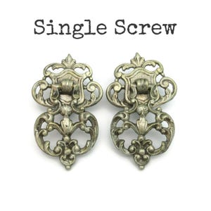 May include: Two antique-style silver drawer pulls with ornate scrollwork and a central floral design. The pulls have a hinged handle and are mounted on a decorative backplate. The text "Single Screw" is above the pulls.