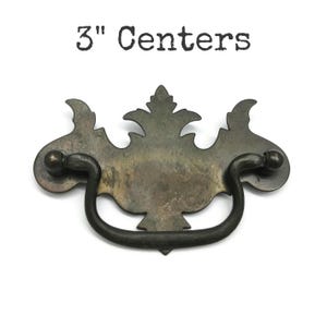 May include: A dark bronze-toned metal drawer pull with a decorative backplate featuring a central leaf-like motif and a curved drop handle. The text 3" Centers is printed above the hardware, indicating the distance between the mounting points.