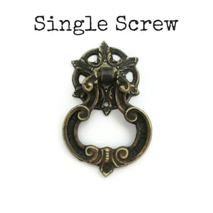 May include: A single ornate brass cabinet pull with a decorative ring handle and a single screw. The pull has a dark patina finish.