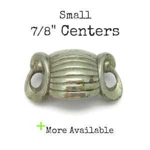 May include: A small, silver-toned metal drawer pull with a ribbed center and loop handles. The text "Small 7/8" Centers" is above the pull, and "More Available" is below.