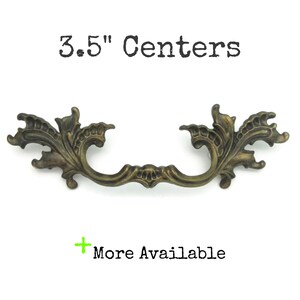 May include: An antique-style drawer pull in a bronze finish, featuring an elaborate floral pattern. The distance between the mounting holes is 8.89 cm. The text "3.5" Centers" is above the pull, and "More Available" is below.
