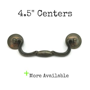 May include: Antique bronze-finished drawer pull with a curved handle and circular backplates. The text "4.5" Centers" is printed above the pull, and "More Available" is printed below. The pull measures 4.5 inches between the centers of the mounting holes.
