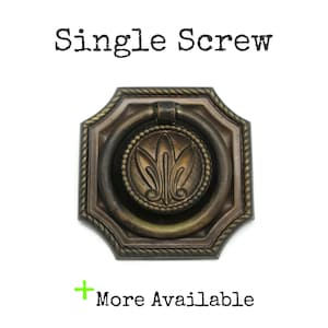 May include: An antique bronze-toned metal drawer pull featuring an octagonal backplate with a rope-style border and a central circular medallion with a fleur-de-lis motif. A round drop handle is attached. Text reads: Single Screw and More Available.