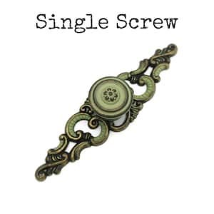 May include: An antique-style cabinet pull with a single screw. The pull features a round, light green center with a floral design, surrounded by ornate, gold-toned metalwork with green accents. The text "Single Screw" is above the pull.