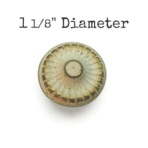 May include: A round, antique-style knob with a diameter of 1 1/8 inches. The knob features a light green and gold color scheme with a central post. The text "1 1/8" Diameter" is printed above the knob.