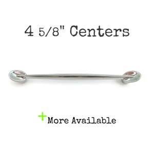May include: A polished silver cabinet pull with oval ends. The text "4 5/8" Centers" is above the pull, and "More Available" is below. This hardware is suitable for drawers and cabinets.