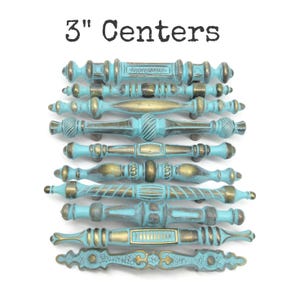 May include: A collection of nine drawer pulls with 3" centers, featuring a distressed turquoise blue finish over a metallic brass base. Each handle displays unique decorative molding, including ribbed, smooth, and rectangular geometric patterns.