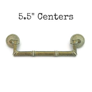 May include: Antique brass drawer pull with a bamboo-style handle and decorative end pieces. The text "5.5" Centers" is printed above the pull. The pull measures 5.5 inches (14 cm) from center to center.