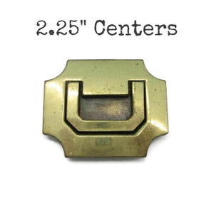 May include: A brass-toned drawer pull with a rectangular backplate and a U-shaped handle. The text "2.25" Centers" is printed above the pull. The hardware has a vintage appearance.