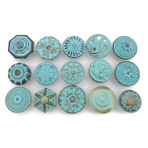 May include: An assortment of antique-style cabinet knobs in various shapes and designs. The knobs feature a distressed turquoise finish with bronze accents. The collection includes round, octagonal, and geometric shapes, perfect for adding a vintage touch to furniture.