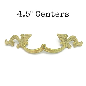 May include: A gold-toned, ornate drawer pull with a curved design. The pull features a decorative, leaf-like pattern on each end and a curved handle. The text "4.5" Centers" is printed above the pull.