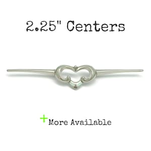 May include: A silver-toned metal cabinet pull with a central heart-shaped design and two pointed horizontal arms. The text 2.25" Centers is printed above the hardware, and a green plus sign with the text More Available is printed below.