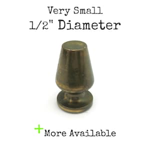 May include: A small, antique brass-colored furniture knob with a conical top and a rounded base. The text "Very Small 1/2" Diameter" is above the knob. The text "More Available" is below the knob.