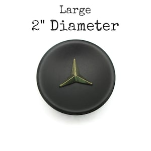 May include: A large, round, matte black button with a 2-inch diameter. Centered on the button is a three-pointed, metallic, brass-toned star emblem. The text "Large 2" Diameter" is printed in black above the button on a white background.