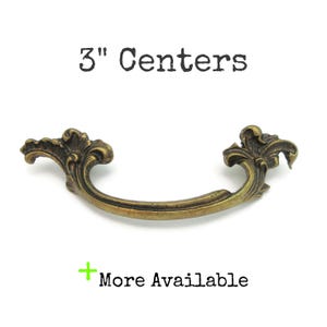 May include: Ornate brass drawer pull with a curved handle and decorative floral accents. The pull measures 7.6 cm between the mounting holes. Text on the image reads "3" Centers" and "More Available".