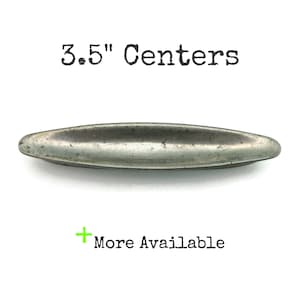 May include: A long, oval-shaped, metal drawer pull with a distressed finish. The text "3.5" Centers" is above the pull, and "More Available" is below. The pull measures 3.5 inches in length.