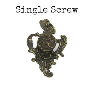 May include: An antique brass-colored metal drawer pull with a central circular knob and an ornate, scrolling backplate featuring leaf-like patterns. The text "Single Screw" is printed in black above the hardware, which has two mounting holes.