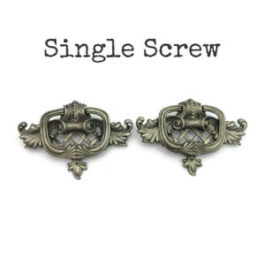 May include: Two antique-style drawer pulls with a silver finish. Each pull features an ornate design with a rectangular handle, a decorative lattice pattern, and leaf accents. The text "Single Screw" is above the pulls.