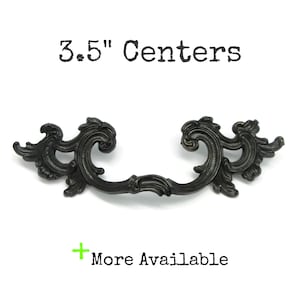 May include: A dark, ornate metal drawer pull with scrolling, leaf-like details and two mounting points. The text 3.5" Centers is printed above the handle, and the text + More Available is printed below the handle in black and green.