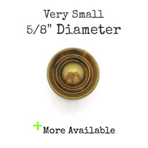 May include: A small, brass-colored, circular object with concentric rings. The text above reads "Very Small 5/8" Diameter" and below "+ More Available". The object has a diameter of approximately 1.59 cm.