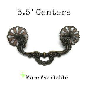 May include: A dark bronze-toned metal drawer pull with a curved handle and two circular, petal-like mounting plates. The text 3.5" Centers is displayed above the hardware, and the text + More Available is displayed below the hardware.