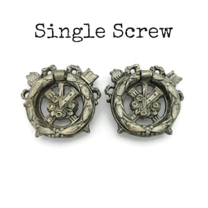 May include: Two antique silver-toned drawer pulls with a decorative wreath design. Each pull features a central design with a handle and the text "Single Screw" above the pulls.