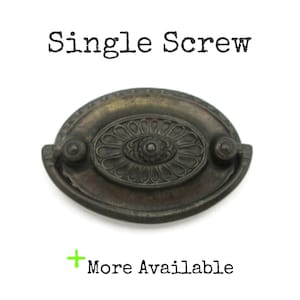 May include: Antique bronze-toned drawer pull with an oval shape and a central floral design. The text "Single Screw" is above the pull, and "More Available" is below. The pull has two small knobs on either side.