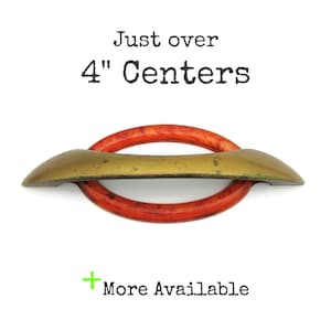 May include: A cabinet pull with a red and gold design. The pull is approximately 4 inches (10 cm) in length. The text "Just over 4" Centers" is printed above the pull. The text "More Available" is printed below the pull.