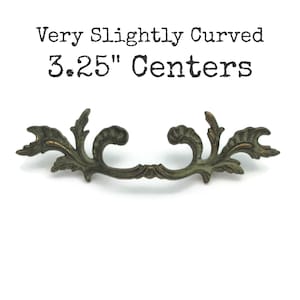 May include: Ornate, antique-style drawer pull with a slightly curved design. The bronze-colored handle features a detailed floral pattern and measures 3.25 inches between the centers of the mounting holes. The text on the image reads "Very Slightly Curved 3.25" Centers."