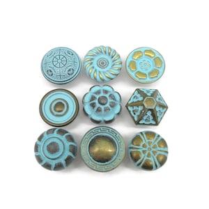 May include: A collection of nine decorative knobs arranged in a three-by-three grid. Each knob features a combination of turquoise blue and antique brass finishes, showcasing various geometric, floral, and circular patterns in relief.
