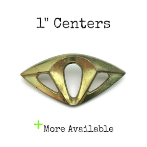 May include: A gold-toned metal decorative hardware piece with a unique, eye-shaped design. The hardware measures 2.5 cm across the center and features an open teardrop shape in the middle. Text on the image reads "1" Centers" and "More Available."
