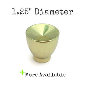 May include: A gold-colored cabinet knob with a conical top and a rounded base. The knob has a diameter of 1.25 inches. The text "1.25" Diameter" is above the knob, and "More Available" is below it.