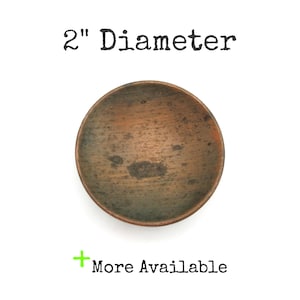 May include: A small, round, copper-colored bowl with a 2-inch diameter. The bowl has a slightly textured surface and a dark patina. The text "2" Diameter" is above the bowl, and "More Available" is below.