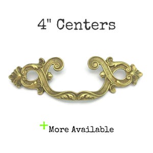 May include: Ornate brass drawer pull with a 4-inch center-to-center measurement. The handle features a curved design with decorative floral and scrollwork details. The text "4" Centers" and "More Available" are displayed.