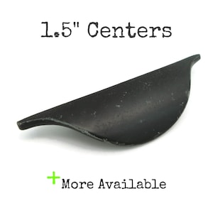May include: A black, curved cabinet pull with a 1.5-inch center-to-center measurement. The text "1.5" Centers" is above the pull, and "More Available" is below. The pull has a matte finish.