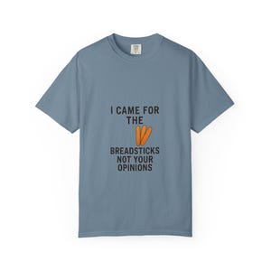 May include: A blue short-sleeve t-shirt with the text "I CAME FOR THE BREADSTICKS NOT YOUR OPINIONS" in black. The word "THE" has an illustration of three orange breadsticks.